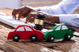 two wooden cars with a gavel next to them and hands on a keyboard typing in the background